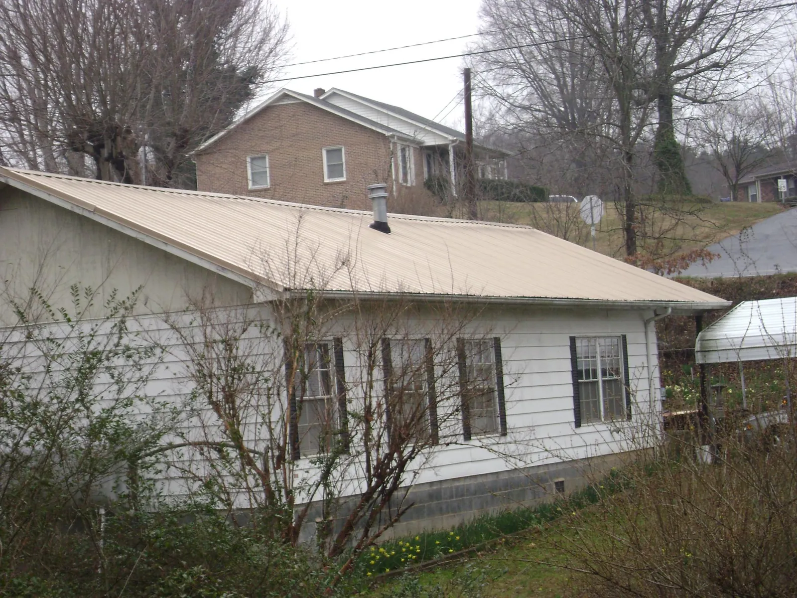 Tan metal roof on a white sided house set into a hillside — Commercial Roofing by Roofing Brothers in Blairstown
